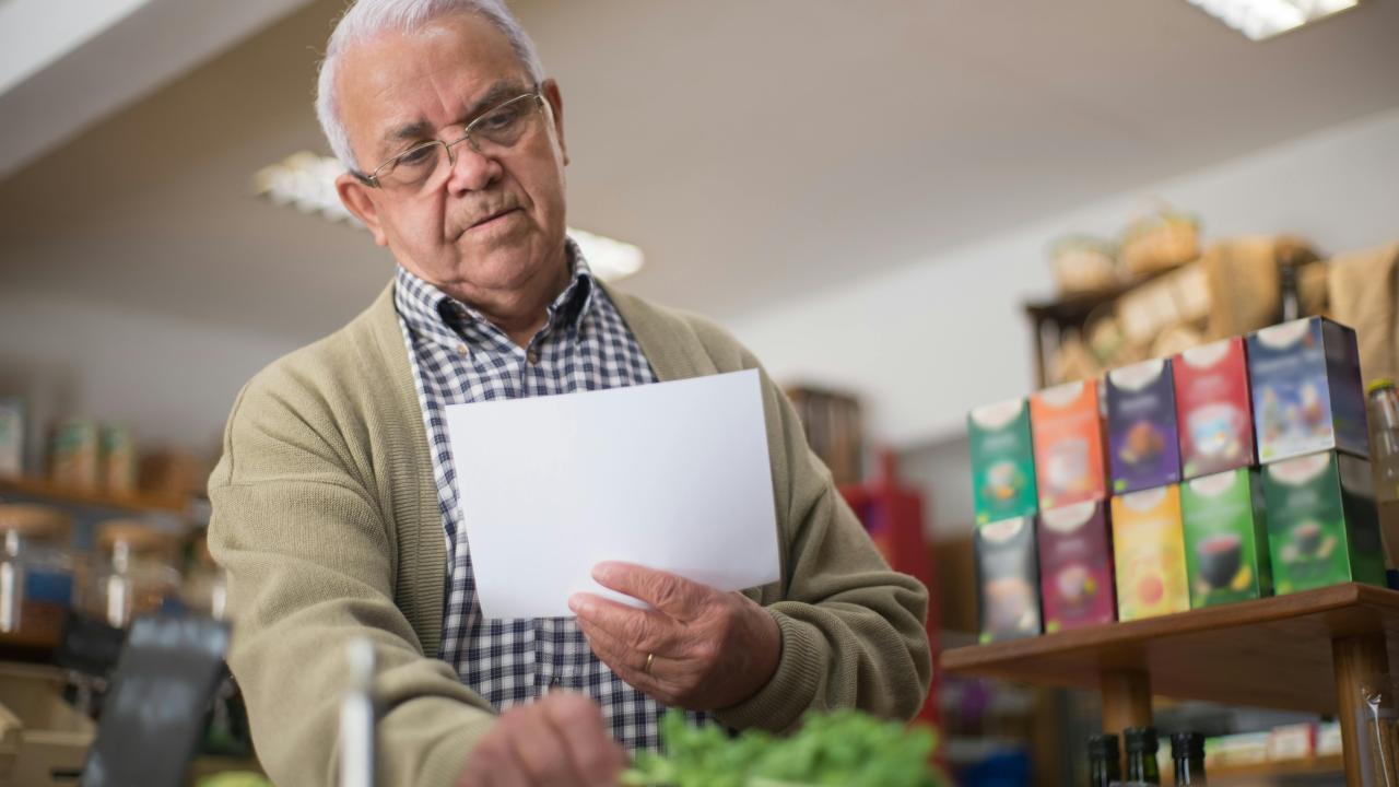 Older shopkeeper in apron checking greens on produce counter, focused expression