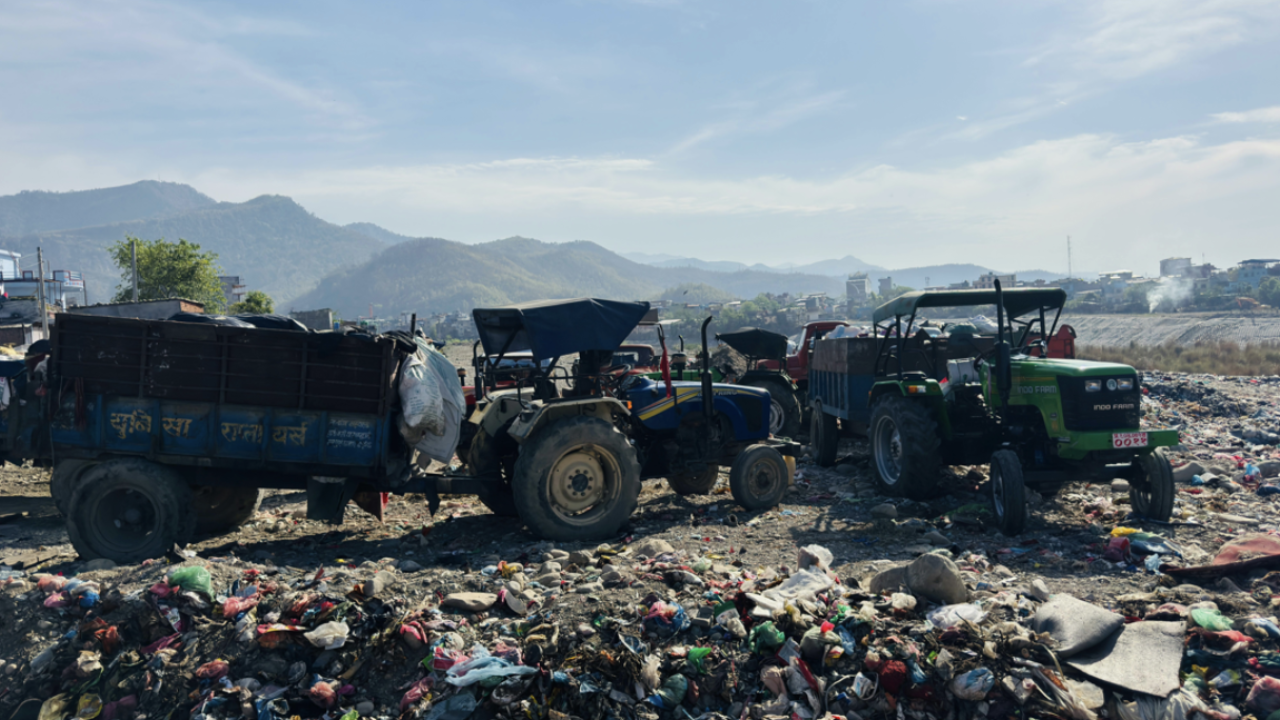 Dump trucks and tractors on a littered landfill with mountains and blue sky