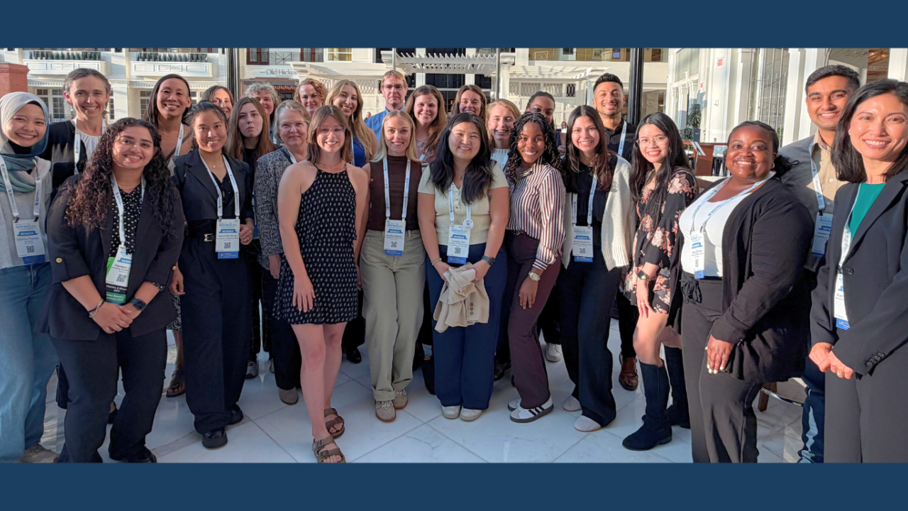 Diverse group of about 30 people smiling on a sunny outdoor terrace, wearing lanyards