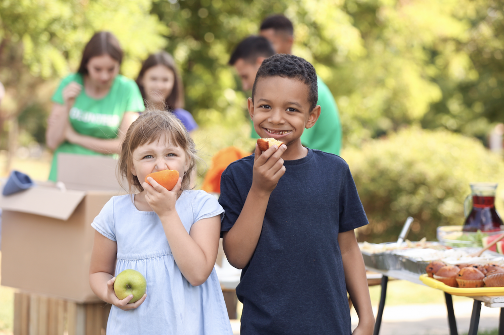 Two smiling kids eating fruit at an outdoor picnic
