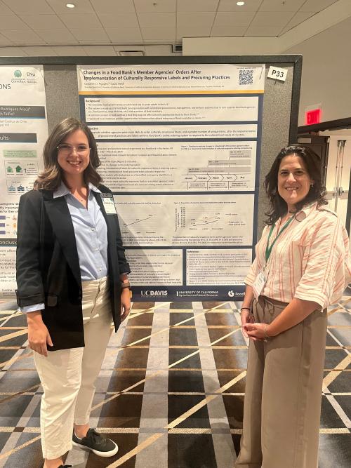 Two women smiling beside a scientific poster at a conference in a carpeted hall