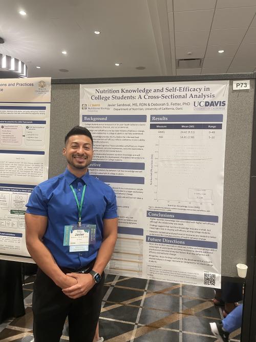 Smiling man in blue shirt standing by a research poster at a conference
