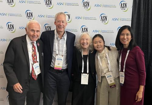 Five smiling adults in business attire posing before a conference logo backdrop