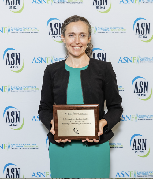 Smiling woman in teal dress holding award plaque before ASN logo backdrop