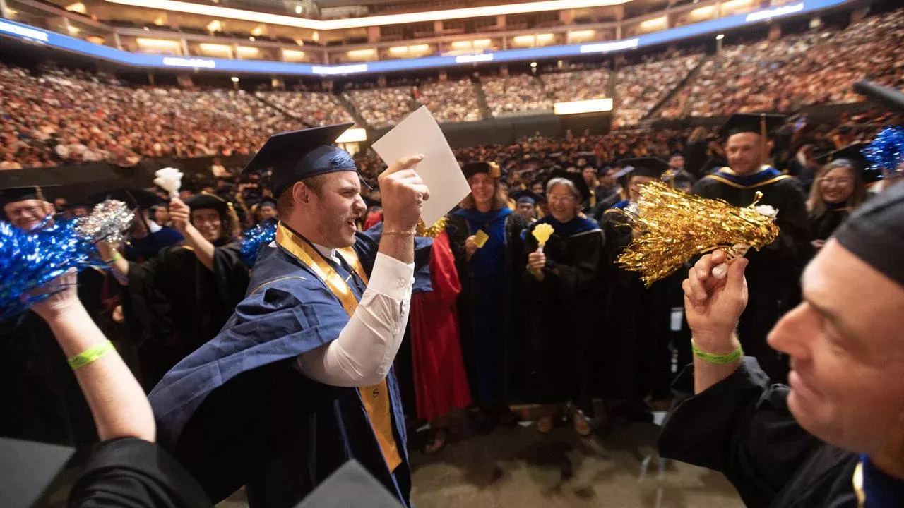 A UCD graduate is crossing the stage to lines of faculty with pompoms and clappers