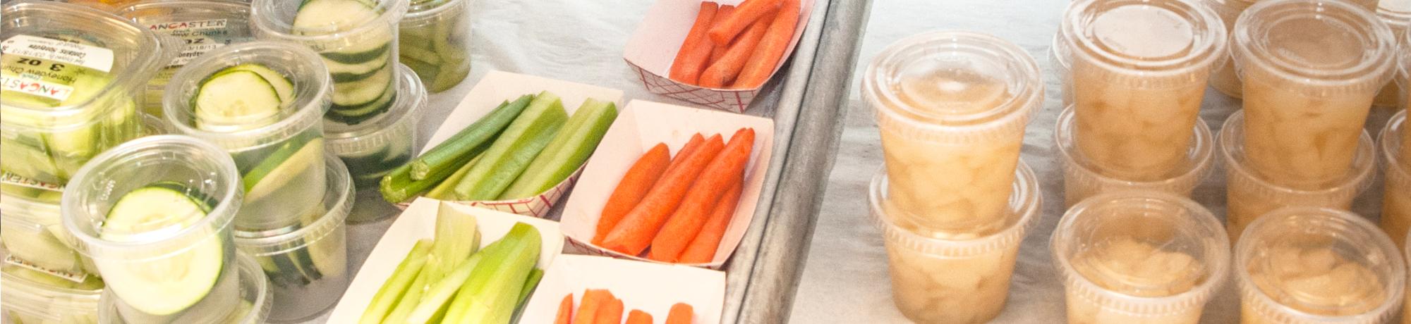 School lunch options, portions of cucumber, celery, carrots, and apple sauce